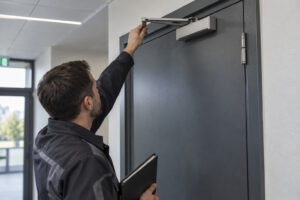 Technicien en maintenance sur une porte coupe-feu et son ferme-porte